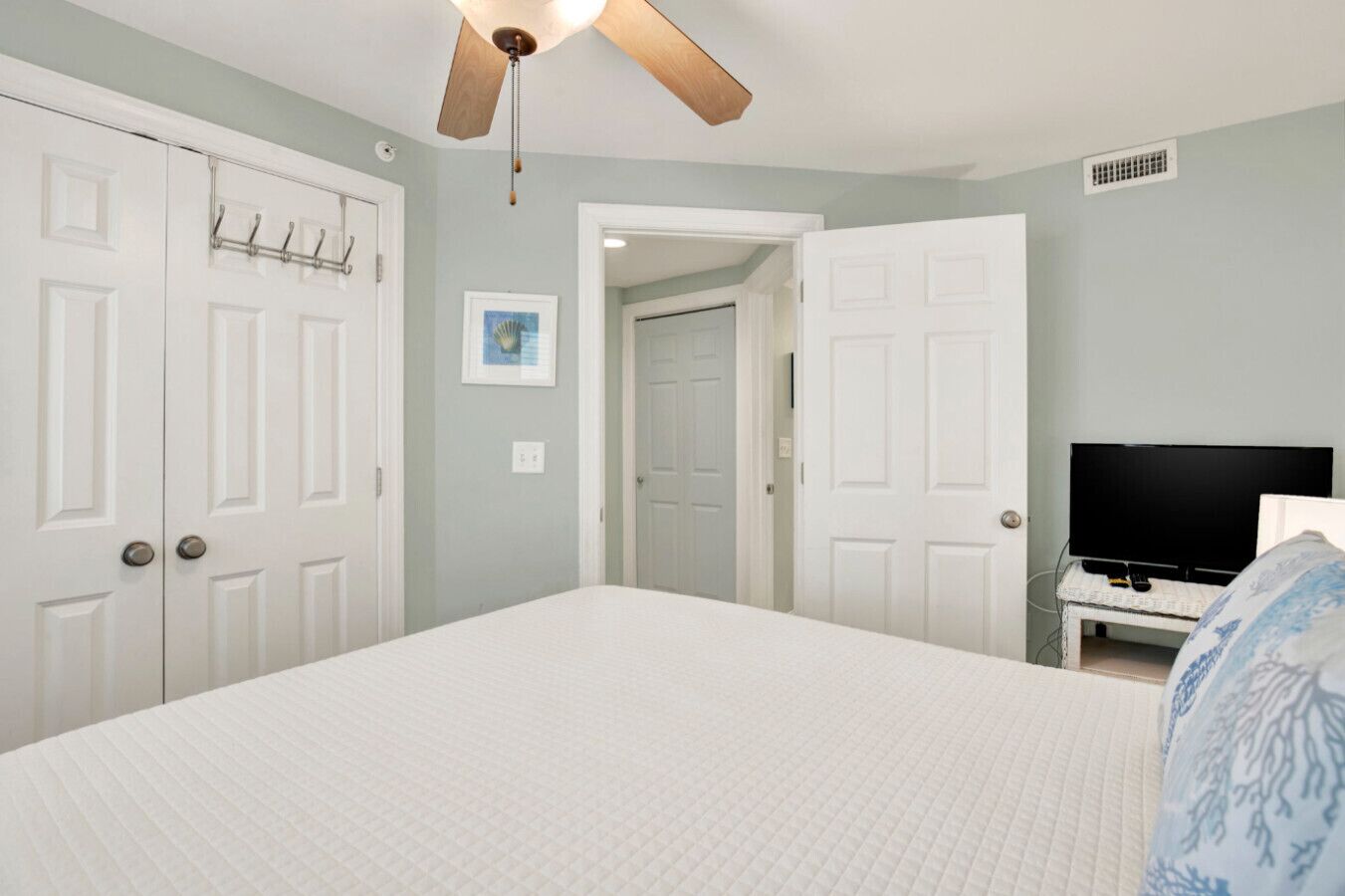 Un dormitorio con cama, ventilador de techo, televisión y puerta que da a otra habitación.