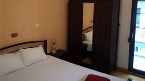 A bedroom with a bed, a wardrobe, a bedside table, and a window. - ALPHA OMEGA   suite (ΑΩ) (Thessaloniki)