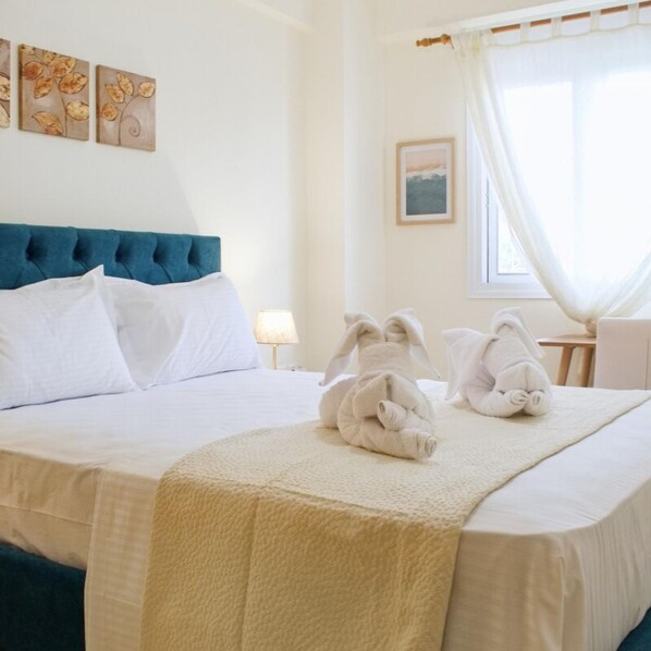 Een net opgemaakt bed met witte lakens, een blauw hoofdbord, en twee handdoeken die op het bed gevouwen liggen.