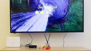 A flat-screen TV mounted on a wall, displaying a nature scene with the text "Super host" and "2023" on the screen. - D&A Sea Breeze next to the sea (Anatolikos Sinikismos)