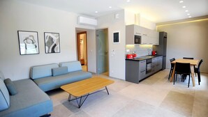 A modern living room with a sofa, coffee table, and dining area with chairs. - Suite Mariengela - Demar Suites (Vlicho)