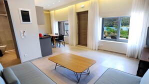 A modern hotel room with a wooden coffee table, grey sofa, and a dining area with a table and chairs. - Suite Mariengela - Demar Suites (Vlicho)