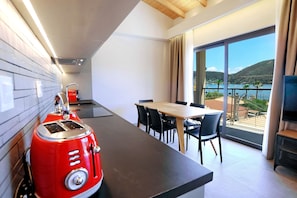 A modern kitchen with a red toaster, a dining area with a table and chairs, and a large window overlooking a scenic view of a lake and hills. - Suite Demi - Demar Suites (Vlicho)