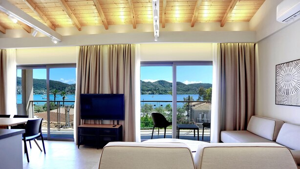 A modern hotel room with a large bed, a TV, a balcony with a view of the sea, and a dining area. - Suite Demi - Demar Suites (Vlicho)