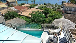 A rooftop pool with a glass barrier, a white umbrella, and a view of a lake with boats and mountains in the background. - Suite Demi - Demar Suites (Vlicho)