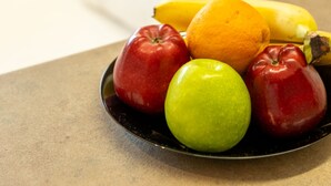 Een fruitschaal op een tafel met appels, een sinaasappel en een banaan.