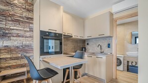 A modern kitchen with a stone accent wall, built-in oven, and a dining area with stools. - Grande Mare with Sea view (Gazi)