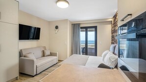 A modern hotel room with a bed, a sofa, a flat-screen TV, a balcony with a view, and a stone accent wall. - Grande Mare with Sea view (Gazi)