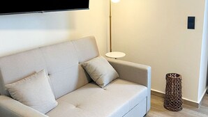 A modern living room with a sofa, a flat-screen TV mounted on the wall, a floor lamp, and a small side table. - Grande Mare with Sea view (Gazi)