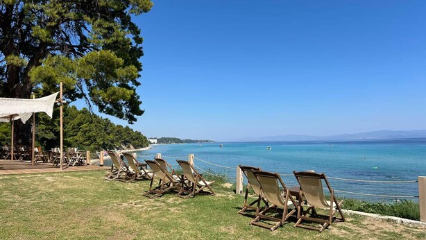 Een strandlounge met houten ligbedden gericht op zee, een gazon en een overkapping.