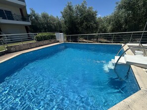 Ein klares, blaues Schwimmbecken mit einer Metallleiter, umgeben von einem Metallzaun und einem Gebäude mit Balkonen.