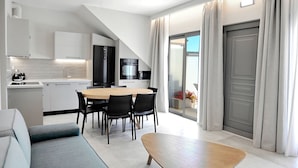 Une cuisine moderne avec des meubles blancs, un coin repas avec une table en bois et des chaises noires, et une porte-fenêtre coulissante donnant sur un balcon.