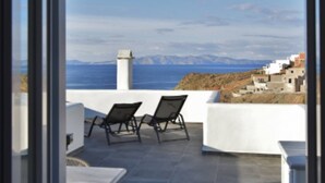Une terrasse avec deux chaises et une table, d’où l’on peut admirer un paysage côtier avec des bâtiments et la mer.