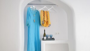 A white room with a blue dress hanging on a rack, a yellow scarf, a wine bottle, and two blue glasses on a shelf. - Tinos Portraits Ano Meria (Exomvourgo)