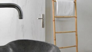 A bathroom with a large, dark stone sink, a bamboo ladder, and a white towel hanging on the wall. - Tinos Portraits Ano Meria (Exomvourgo)