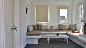 A modern living room with a built-in bench, a small table, and a view of the city through large windows. - Tinos Portraits Kato Meria (Exomvourgo)