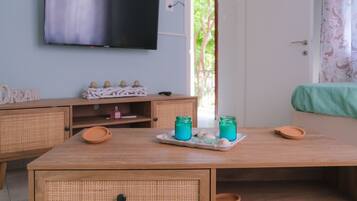 A room with a wooden table, wicker furniture, a flat-screen TV, and a view of greenery outside.