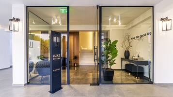 Entrada de un hotel con mostrador de recepción, puerta de cristal y un cartel que dice 'LUAZ SUITES'.