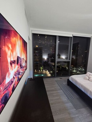 A modern bedroom with a large TV, a bed, and a view of a cityscape at night. - Miami-Brickell Luxury 2BR-2BATH with skyline VIEWS (Miami)