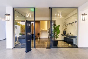 Entrada de un hotel con puerta de vidrio, una recepción y un letrero que dice 'LUAZ SUITES'.