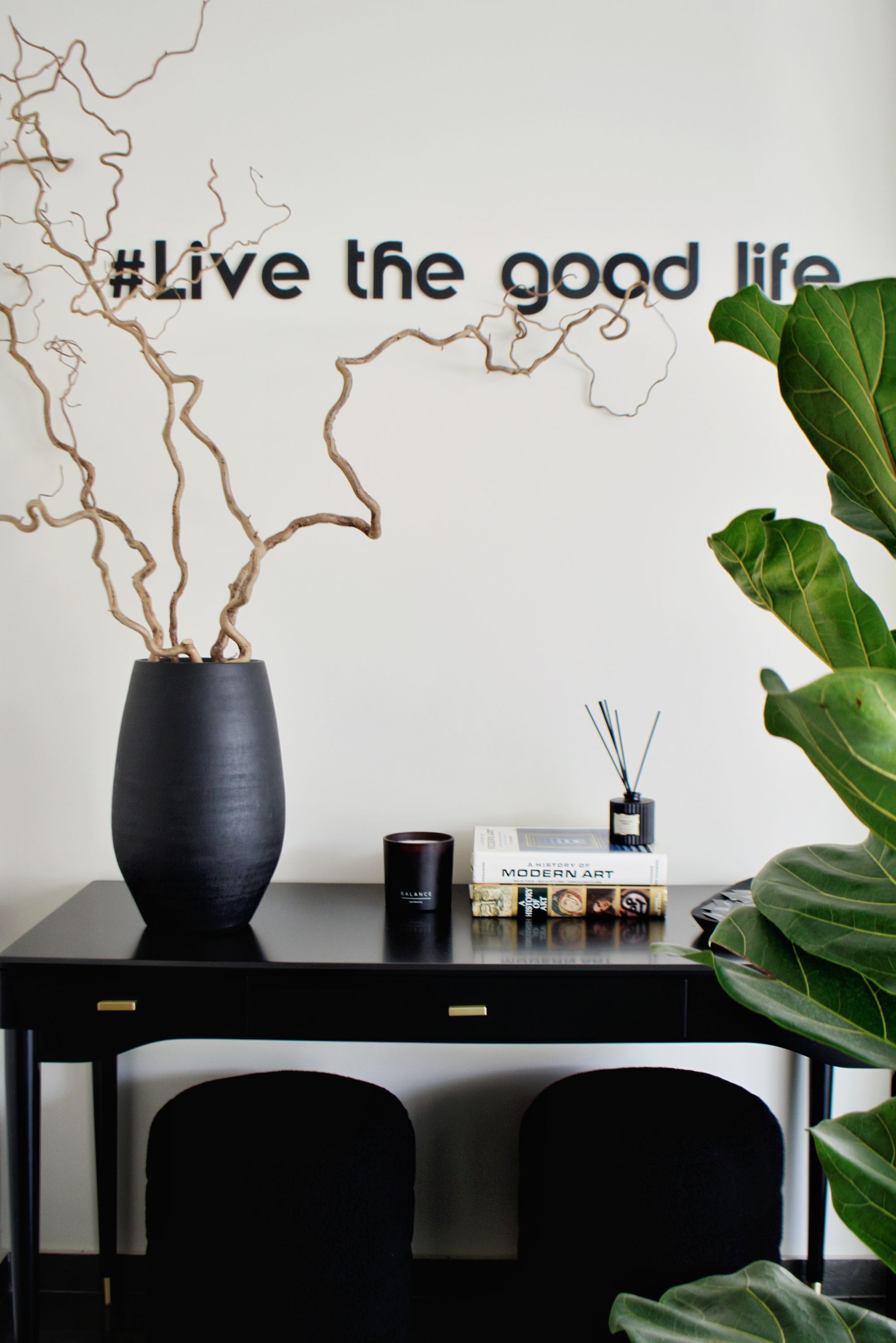 A desk with a black vase, a book titled 'A History of Modern Art,' and a wall with the phrase '#Live the good life'.