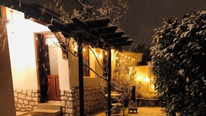 Ett snötäckt utomhusområde med en stenmur, en träpergola och en bänk.