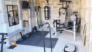 Ett utomhusgym under tak med träningsredskap, ett löpband och en boxningssäck.
