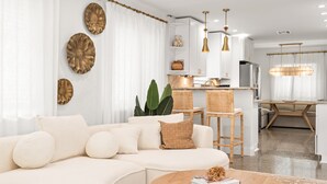 Una sala de estar moderna con un sofá blanco, una mesa de centro de madera y una cocina al fondo.