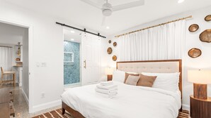 Un dormitorio moderno con una cama grande, ventilador de techo y vistas al baño.