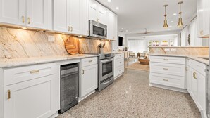 Una cocina moderna con armarios blancos, encimeras de granito, electrodomésticos de acero inoxidable e iluminación colgante.