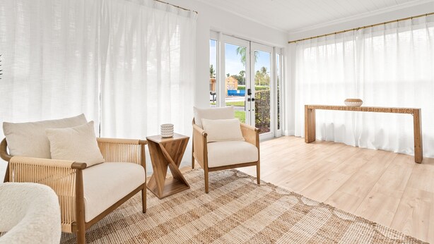 Una habitación amplia con un gran ventanal, un ventilador de techo y piso de madera.