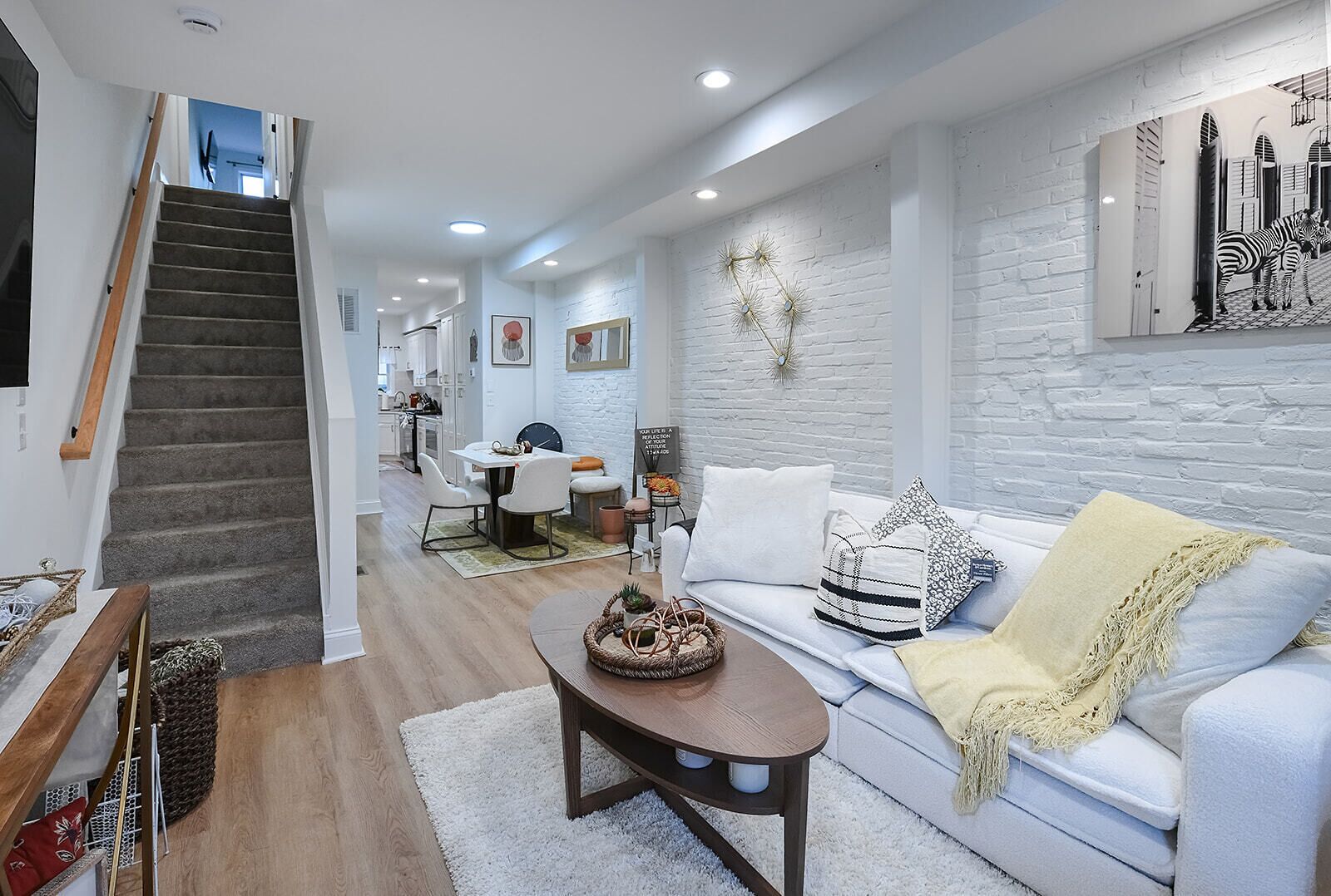 Uma sala de estar moderna com escada, paredes de tijolo branco e uma área de jantar ao fundo.