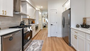 A modern kitchen with white cabinets, stainless steel appliances, and a wooden floor.