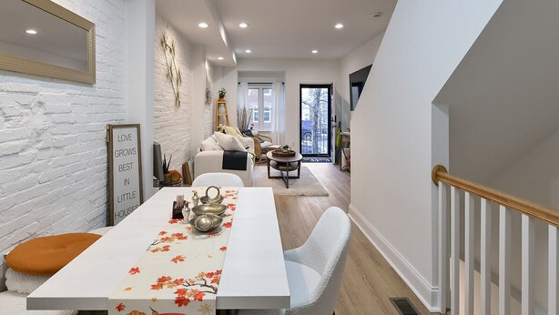 A modern kitchen with a dining area, white brick walls, and a staircase leading to an upper level.