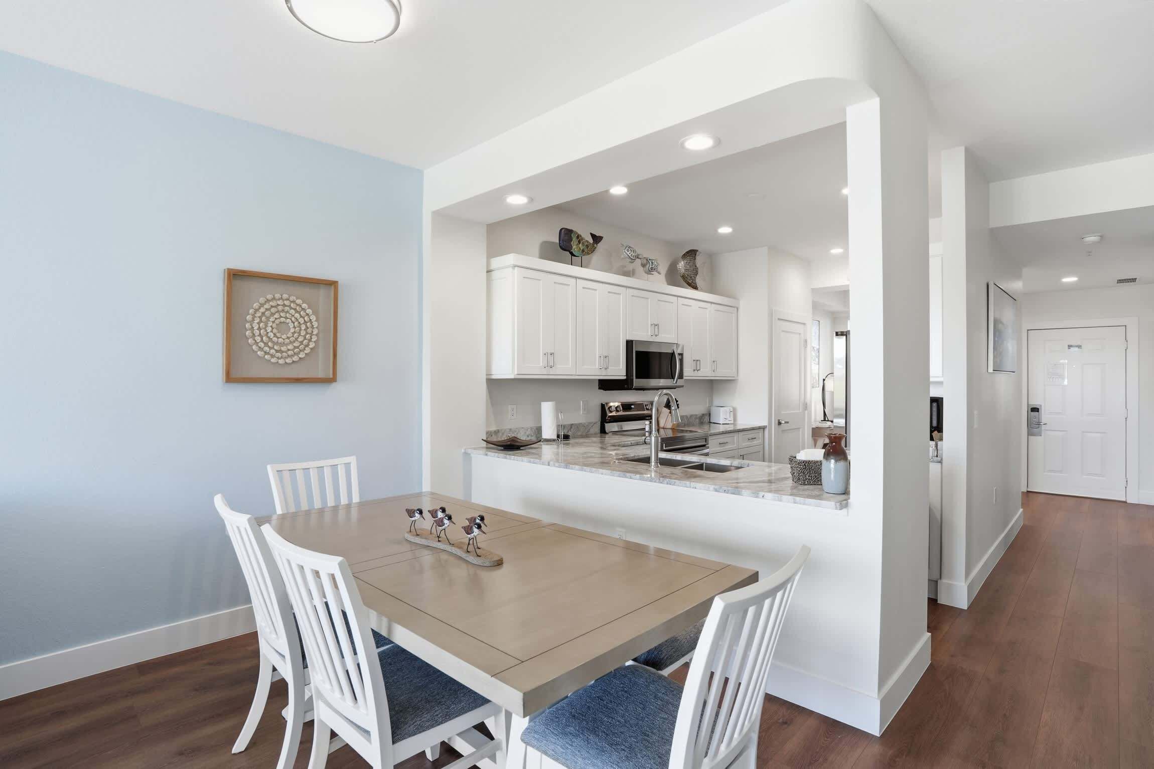 A modern kitchen with white cabinetry, a central island, and a dining area with a wooden table and white chairs.