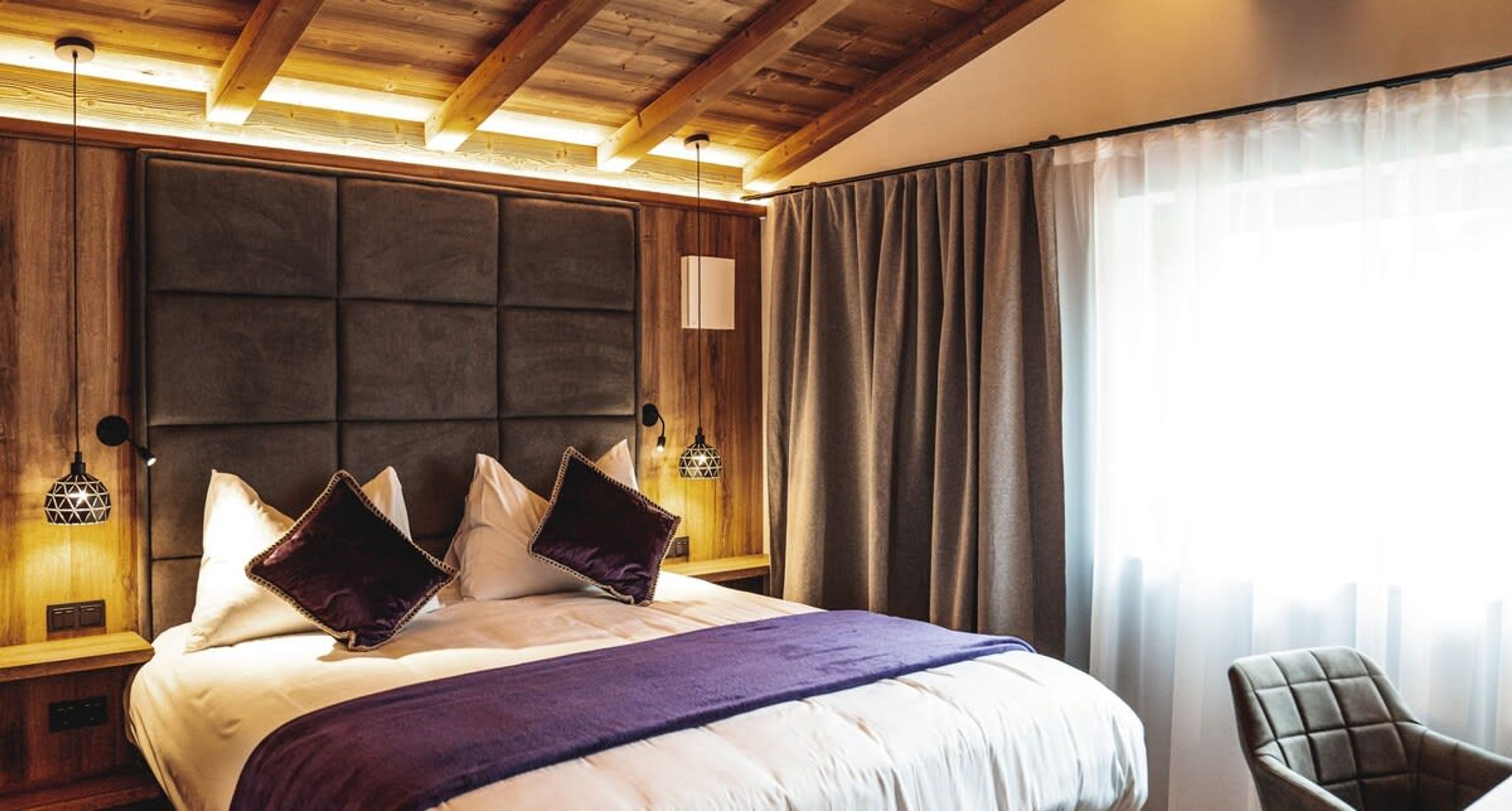 Une chambre d’hôtel avec un grand lit, une tête de lit en bois, deux lampes de chevet et une chaise.