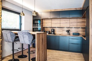 A modern kitchen with wooden cabinets, a bar area with two bar stools, and pendant lighting. - Chalet Amadeus - Designer Luxury Chalet for 14 (Piesendorf)