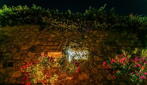 Mur de pedra amb un rètol que diu "Villa Avia" i vegetació al voltant.