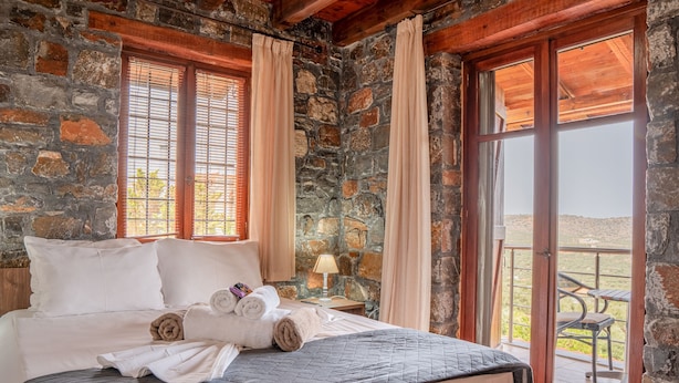 Ein Zimmer mit steinernen Wänden, einem Bett, Vorhängen und Blick durch eine Glastür.