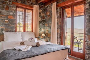 Een kamer met stenen muren, een bed, gordijnen en uitzicht door een glazen deur.