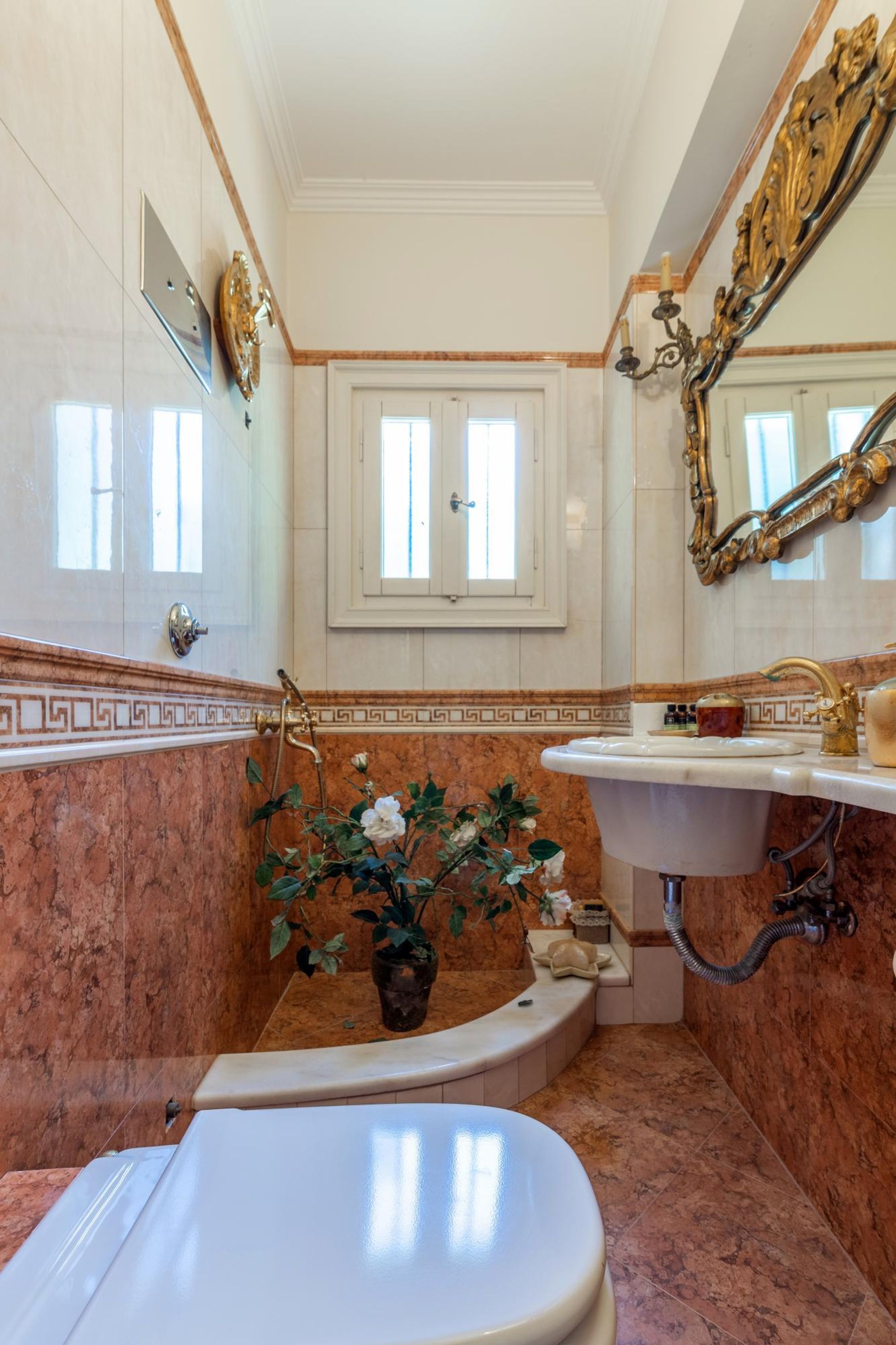 Ein Badezimmer mit Marmorboden, einer weißen Badewanne, einem weißen Waschbecken und einem großen Spiegel mit goldener Rahmung.