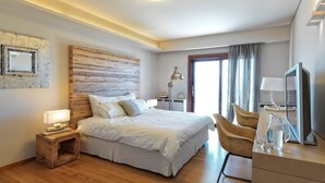 Habitació d'hotel moderna amb un panell de capçalera de fusta, un llit amb roba de llit blanca, una taula de treball amb una cadira, una televisió i una tauleta de nit amb una làmpada.