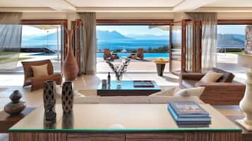 A spacious living room with a glass coffee table, comfortable seating, and a view of the ocean and mountains.