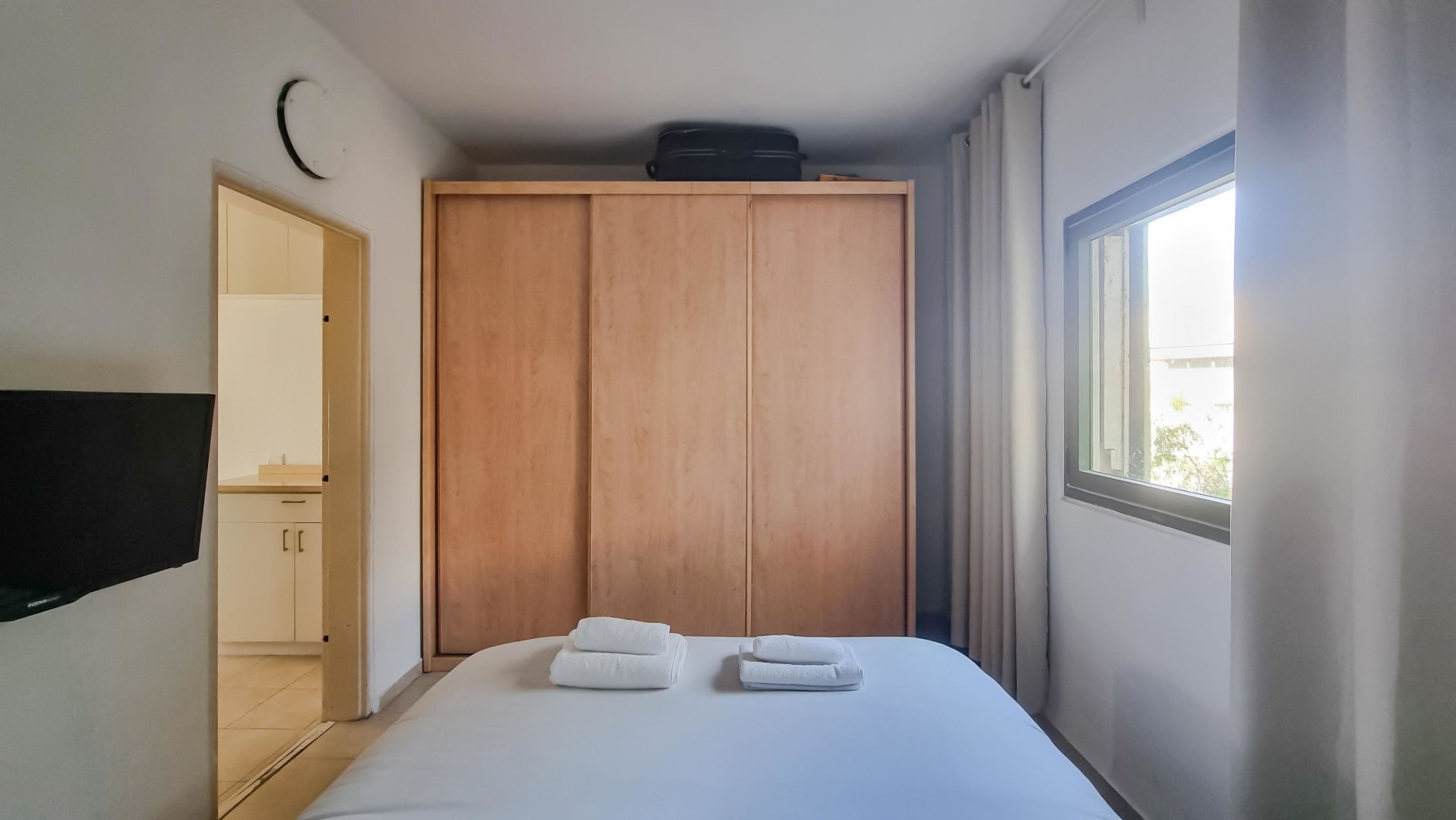 A bedroom with a bed, a wardrobe, a TV, and a window.