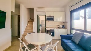 A compact kitchen with a microwave, stove, and sink. There is a dining table with chairs and a blue sofa with a pillow. A staircase leads to another room. - Ben Yehouda Obsidian (Tel Aviv-Yafo)