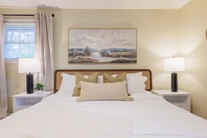 Quarto de hotel com uma cama grande, duas mesas de cabeceira com abajures, um quadro na parede e uma janela com cortinas.