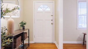 A hallway with wooden flooring, a white door, a console table with baskets, a lamp, and a potted plant. - Epic Game Room Hangout with Grill, King Beds & 5 TVs (Valdosta)