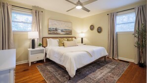 A bedroom with a bed, nightstands, a ceiling fan, a painting, and a potted plant. - Epic Game Room Hangout with Grill, King Beds & 5 TVs (Valdosta)