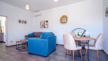 A modern living room with a blue sofa, a small table, and a dining area with chairs.