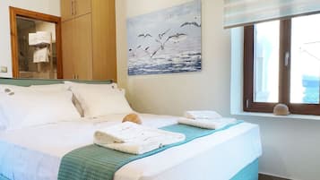 Une chambre à coucher avec un lit, des poutres en bois au plafond, un tableau représentant des oiseaux, une fenêtre donnant sur un paysage et un sol carrelé.
